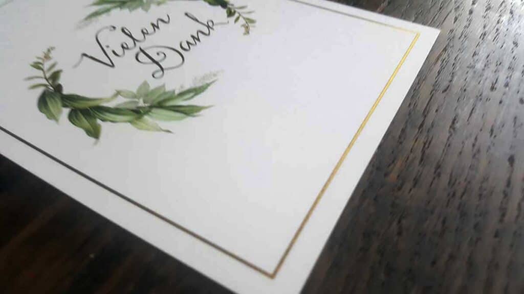 a white card with green leaves and a gold border